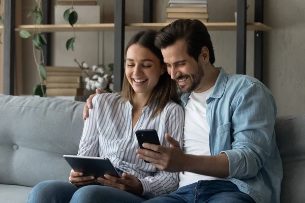 Lächelndes Paar entspannt sich auf Sofa mit Gadgets — Stockfoto
