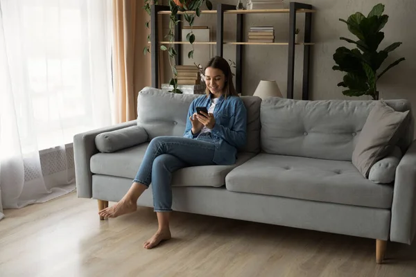 Jeune femme se détendre sur le canapé en utilisant un smartphone — Photo