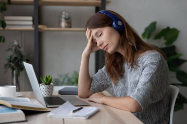 Çalışma masasında oturan kulaklıklı genç kadın bunalmış..