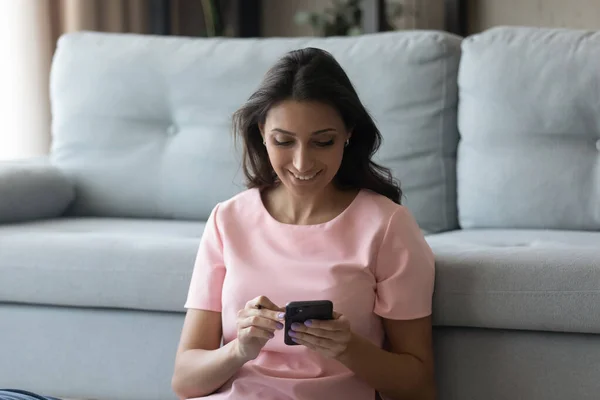 Femme multiraciale millénaire souriante utilisant des smartphones, assise sur le sol. — Photo