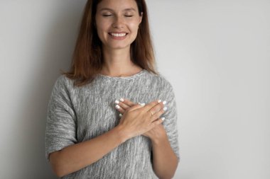 Gülümseyen genç bir kadın ellerini göğsüne katlamış, minnet duyuyor..