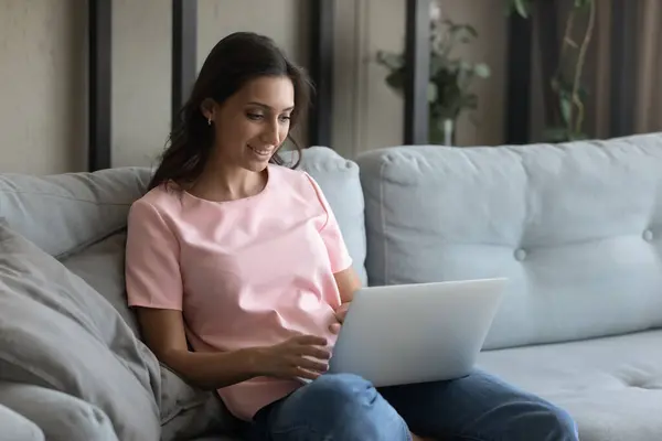 Sorridente giovane donna razza mista utilizzando il computer, seduto sul divano. — Foto Stock