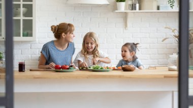 Gülümseyen anne ve iki küçük kız birlikte salata pişiriyorlar.