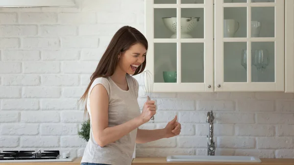 Dolblij grappige jonge vrouw zingen in garde, staan in de keuken — Stockfoto