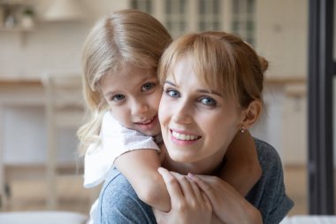 Sırtında küçük bir kızı taşıyan gülümseyen anne portresi.