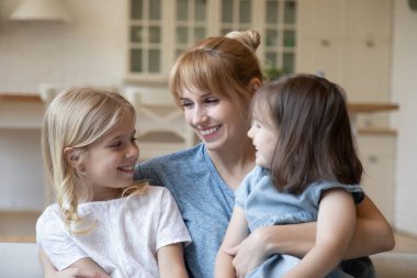 Gülümseyen bir anne, iki küçük kızı kucaklıyor.