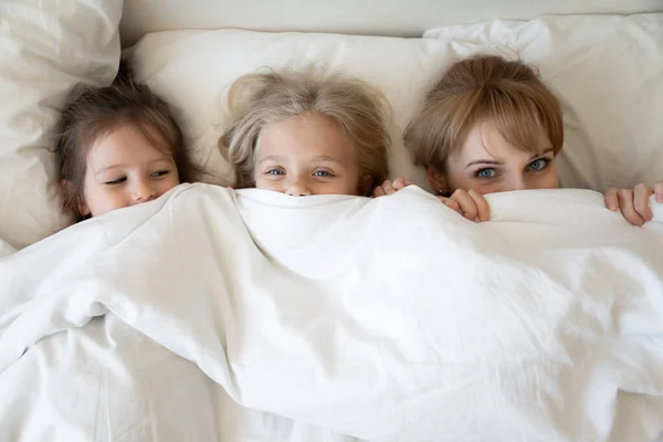 Top melihat ibu dan dua putri menggemaskan mengintip dari selimut — Stok Foto