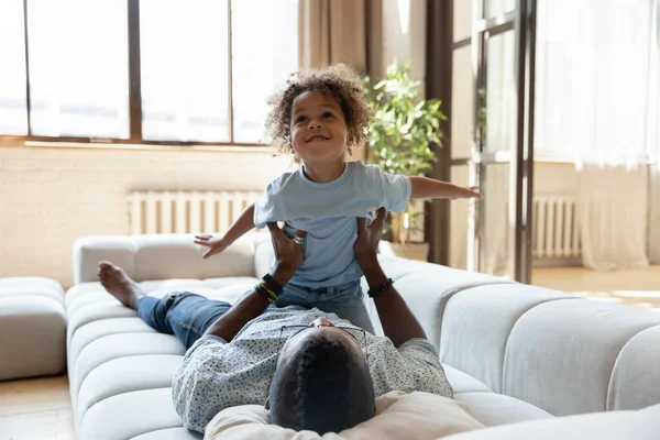 Lachender schwarzer Ziehvater und Adoptivsohn spielen auf Sofa — Stockfoto