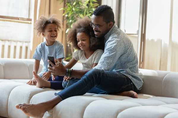 Père africain et deux enfants regardant des dessins animés drôles sur téléphone portable — Photo