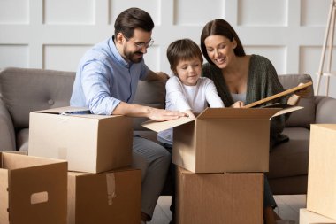 Küçük çocuklu mutlu aile taşınma gününde kutuları boşaltıyor.