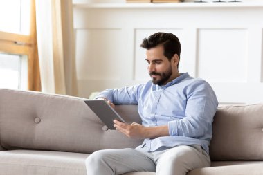 Kafkasyalı genç adam evdeki kanepede tabletle rahatlıyor.