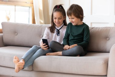 Mutlu çocuklar evdeki kanepede cep telefonuyla rahatlar.