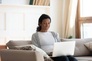 Afrikalı Amerikalı kadın bilgisayar kullanarak kanepede dinleniyor.