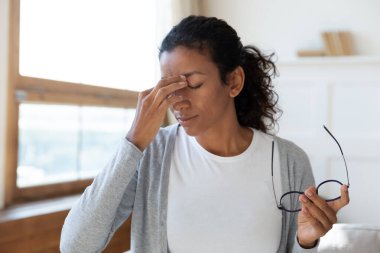 Yorgun melez kadın migrenden muzdarip gözlüğünü çıkarıyor.