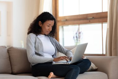 Afro-Amerikalı kadın evde dizüstü bilgisayar kullanarak rahatlıyor