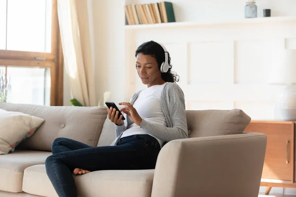 Mujer afroamericana en auriculares usan teléfono inteligente en casa — Foto de Stock