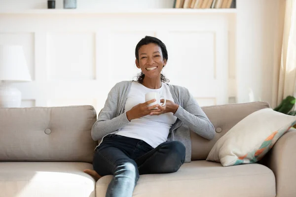 Retrato de mujer birracial sonriente relajarse en el sofá en casa — Foto de Stock