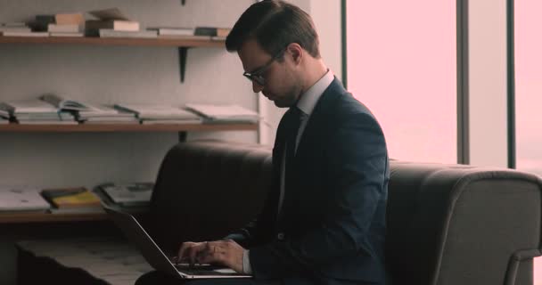 Obchodník ve formalsuit sedět v kanceláři pomocí notebooku textové e-maily — Stock video