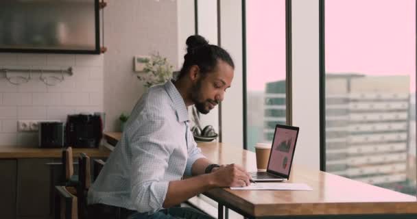 Afrikaanse zakenman met laptop met grafieken en gegevens op het scherm — Stockvideo