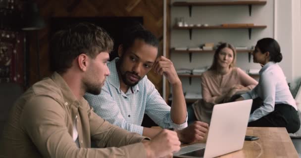 Багатоетнічні чоловіки-колеги сидять в коворкінгу, використовуючи ноутбук обговорюють завдання — стокове відео