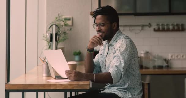 Focused african businessman holding papers typing on laptop preparing report — стокове відео