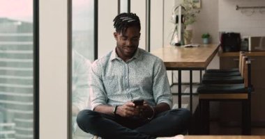 African guy using smartphone resting in modern skyscraper office room