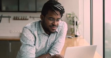 Serious african man do telecommute job using laptop in kitchen