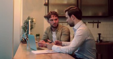 Meslektaşlar ofis mutfağında birlikte oturup kablosuz bilgisayar kullanarak çalışırlar.