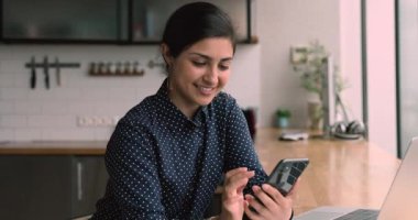 Çekici Hintli kadın mutfakta akıllı telefon cihazıyla oturuyor.