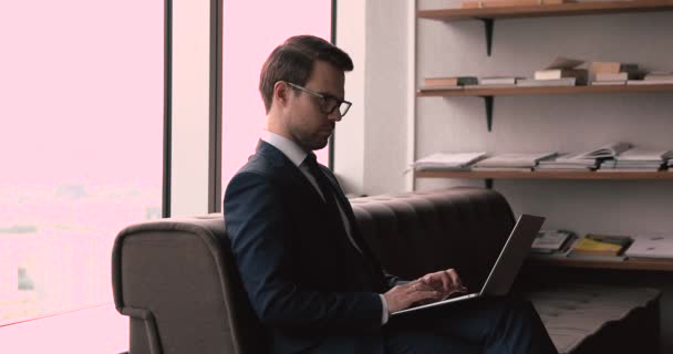 Серьезный бизнесмен сидит в офисе, используя электронную почту с ноутбуком — стоковое видео