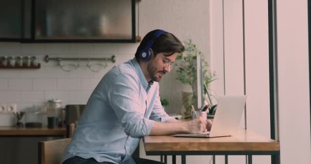 Homem usar fones de ouvido escuta áudio palestra on-line estudando em casa — Vídeo de Stock