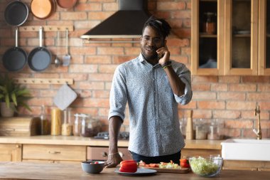 Gülümseyen genç melez adam telefona cevap veriyor, yemek hazırlıyor..
