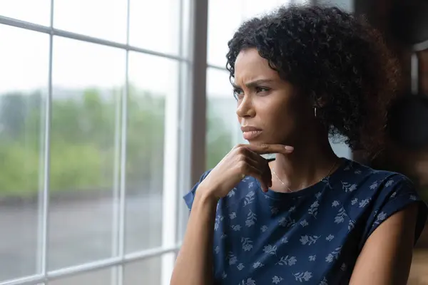 Pensive young african ethnicity woman looking out of window. — Stockfoto