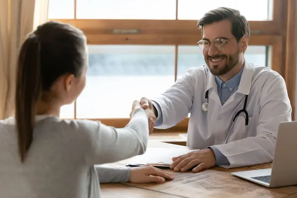 Leende manlig läkare handskakar kvinnlig patient vid mötet — Stockfoto