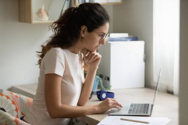 Ciddi kadın gözlük takıyor, dizüstü bilgisayar kullanıyor, proje üzerinde çalışıyor.