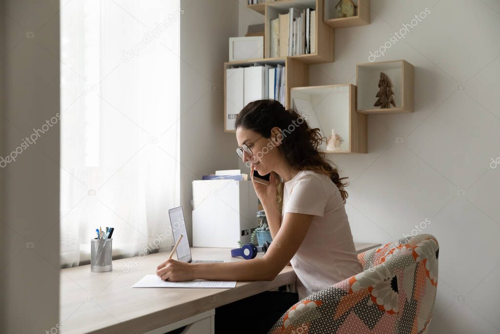 Businesswoman wearing glasses making phone call, writing notes, consulting client