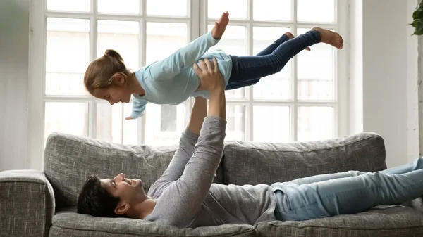 Улыбающийся молодой отец поднимает смеющегося ребенка в воздух. — стоковое фото