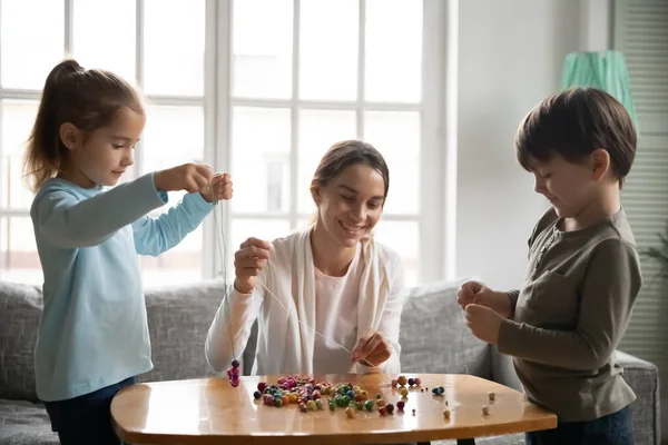 Gelukkig millennial zorgzame mama maken armbanden met kleine kinderen. — Stockfoto