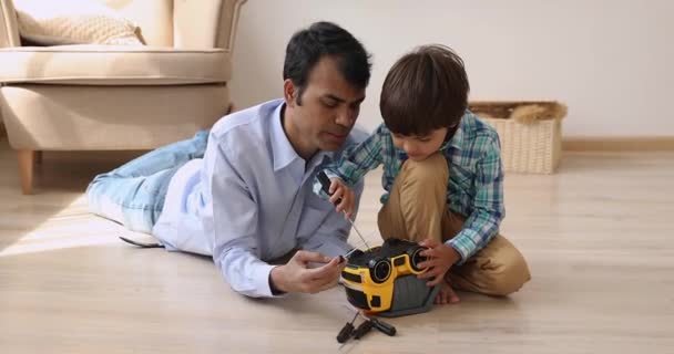 Indyjski ojciec z syn naprawy zabawka samochód grać razem wewnątrz — Wideo stockowe
