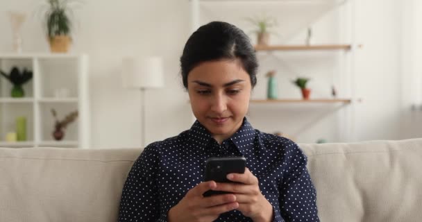 Індійка сидить на дивані, користуючись мобільним телефоном. — стокове відео