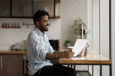 Gülümseyen melez adam dizüstü bilgisayarda kağıt okuyor.