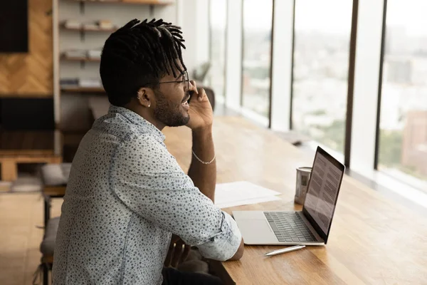 Sourire homme biracial travailler sur ordinateur portable parler sur la cellule — Photo