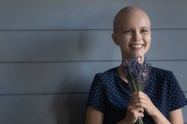 Saçsız, gülümseyen, elinde çiçekler olan bir kanser hastası.