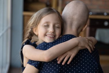 Gülümseyen küçük kız, hasta tüysüz anneye sarılıyor.