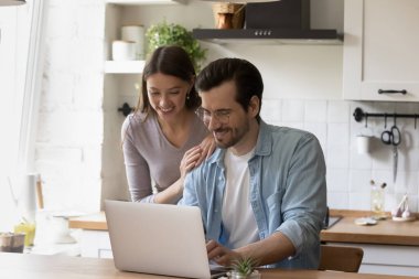 Modern mutfakta dizüstü bilgisayar kullanan mutlu genç çift.
