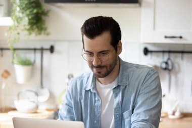 Mutfakta dizüstü bilgisayar kullanarak kendine güvenen gözlüklü adamı kapat.