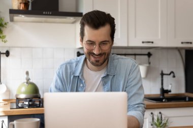 Mutfakta dizüstü bilgisayar kullanarak gülümseyen gözlüklü adamı kapat.