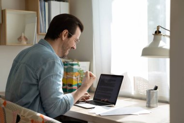 Gözlüklü neşeli iş adamı dizüstü bilgisayara bakıyor, başarıyı kutluyor.