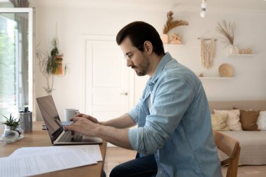 Yan görüş: Gözlüklü ciddi bir adam dizüstü bilgisayarla çalışıyor.