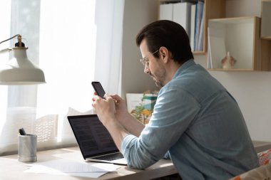 Gözlük takan ciddi bir işadamı akıllı telefon kullanıyor, bilgi arıyor.